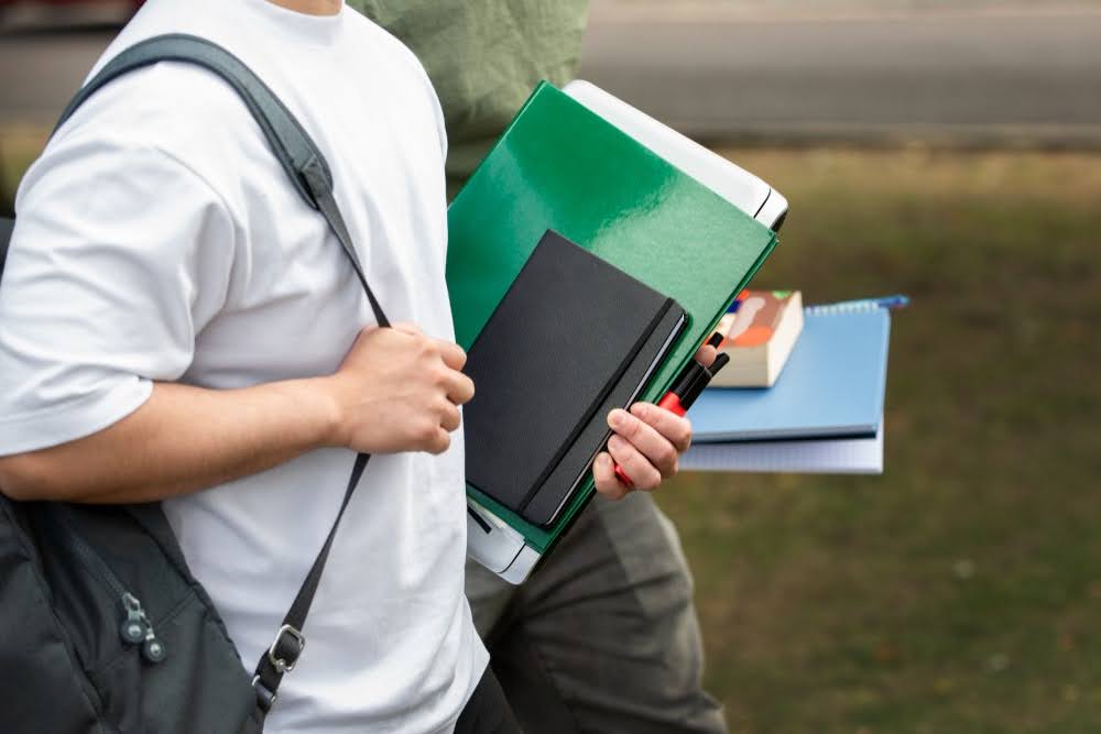 Alunos em instituição de ensino com cadernos e mochilas