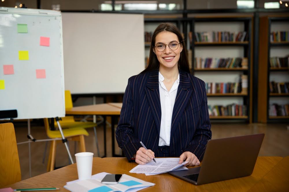 Contado einserida em uma instituição de ensino, com documentos, notebook e livros ao redor